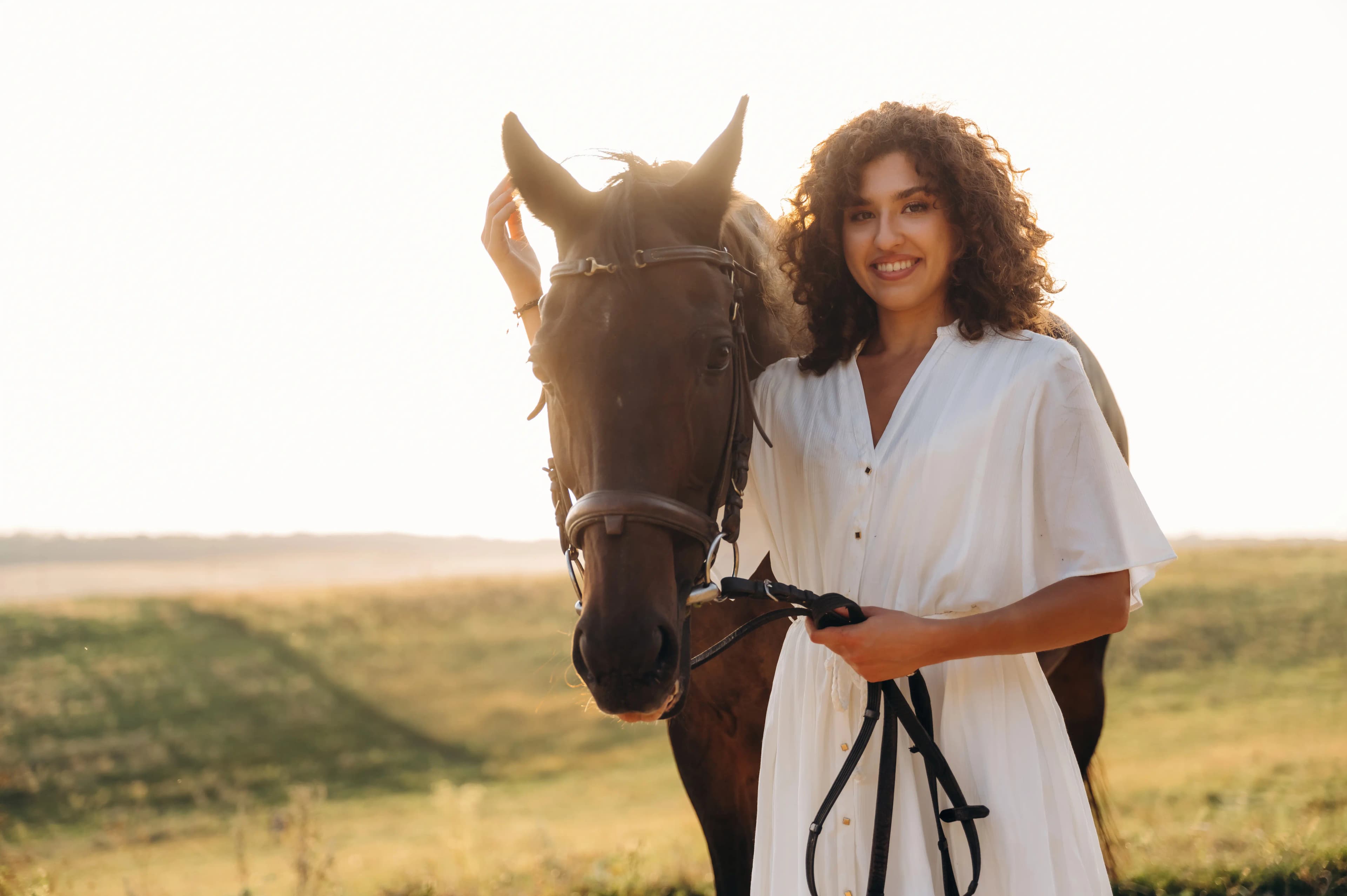A woman standing beside her horse against an open countryside horizon