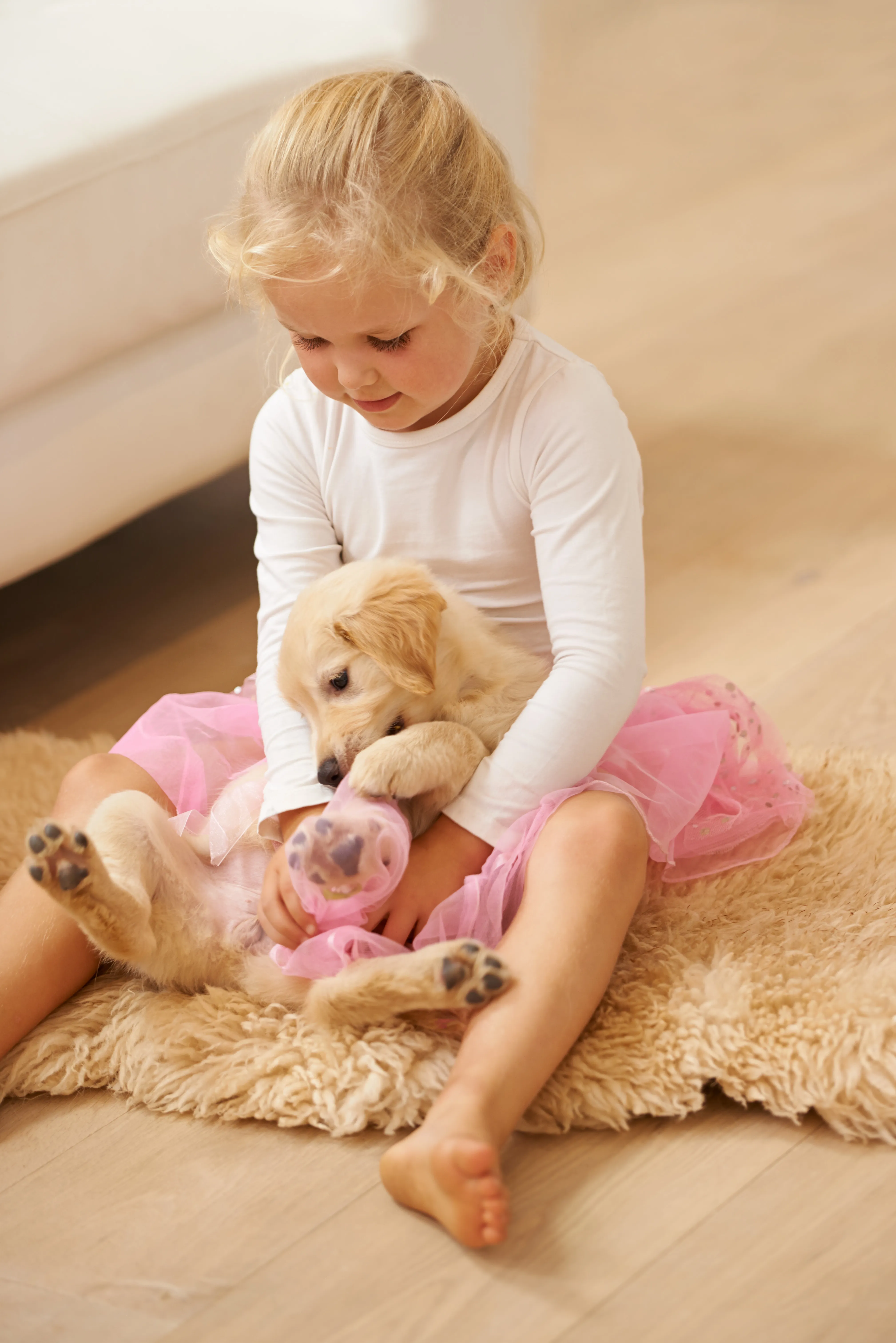 A young girl embracing her golden retriever puppy on a soft rug