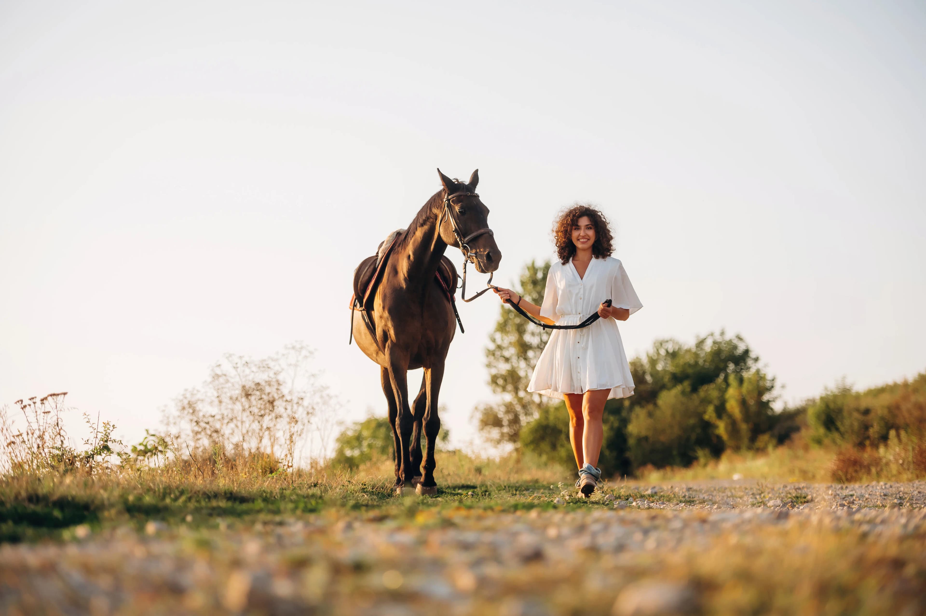 A woman walking with her horse through an open countryside landscape