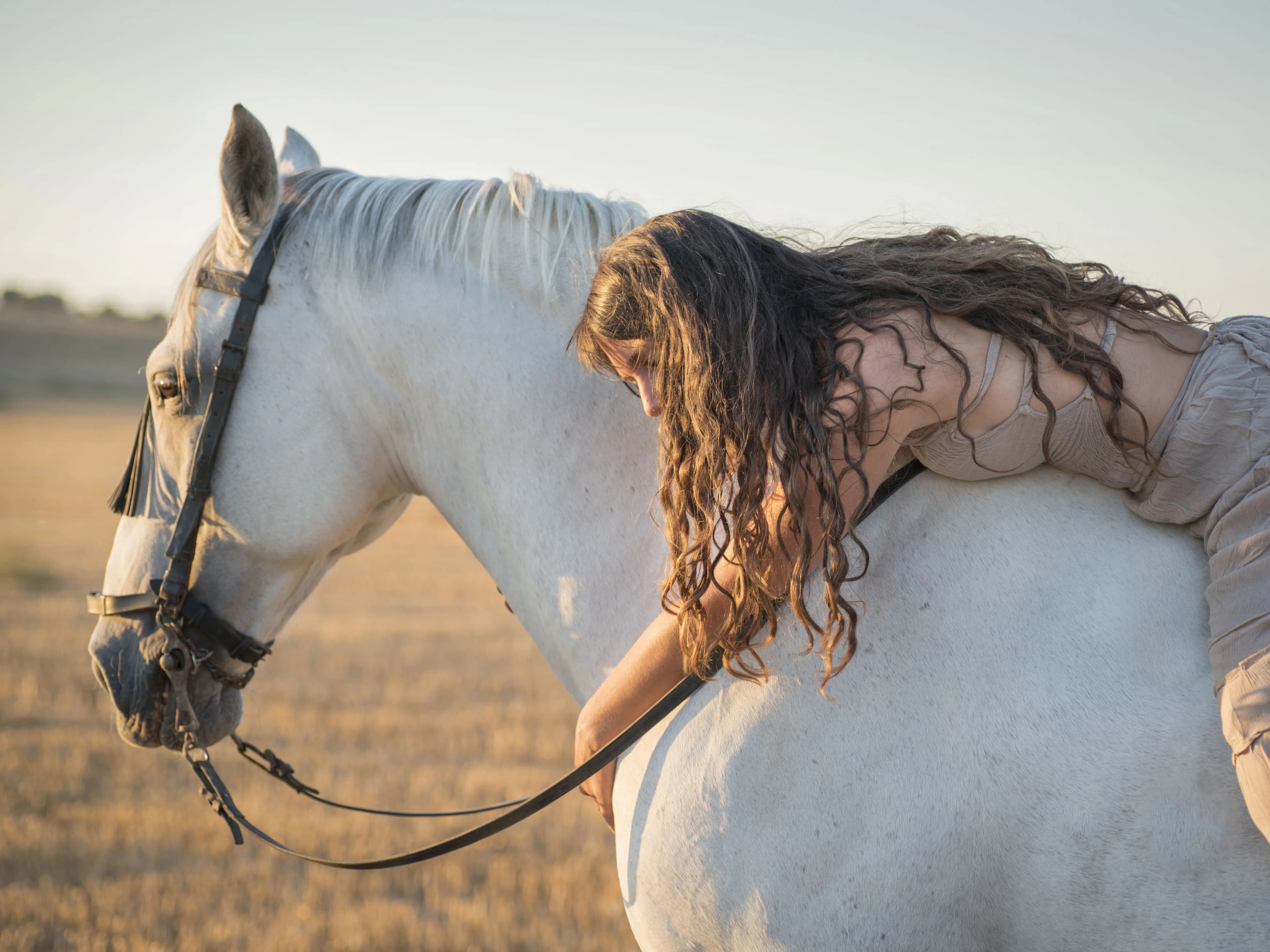 Woman embracing a white horse during an outdoor equestrian photography session